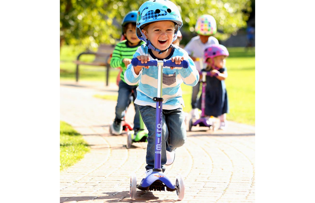 Kid riding a Mini Micro Deluxe Scooter at a park 

