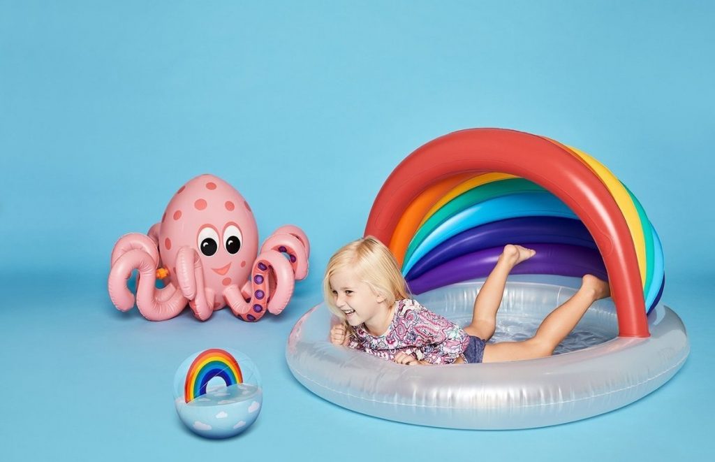 Child paddling on a rainbow inflatable pool by Sunnylife